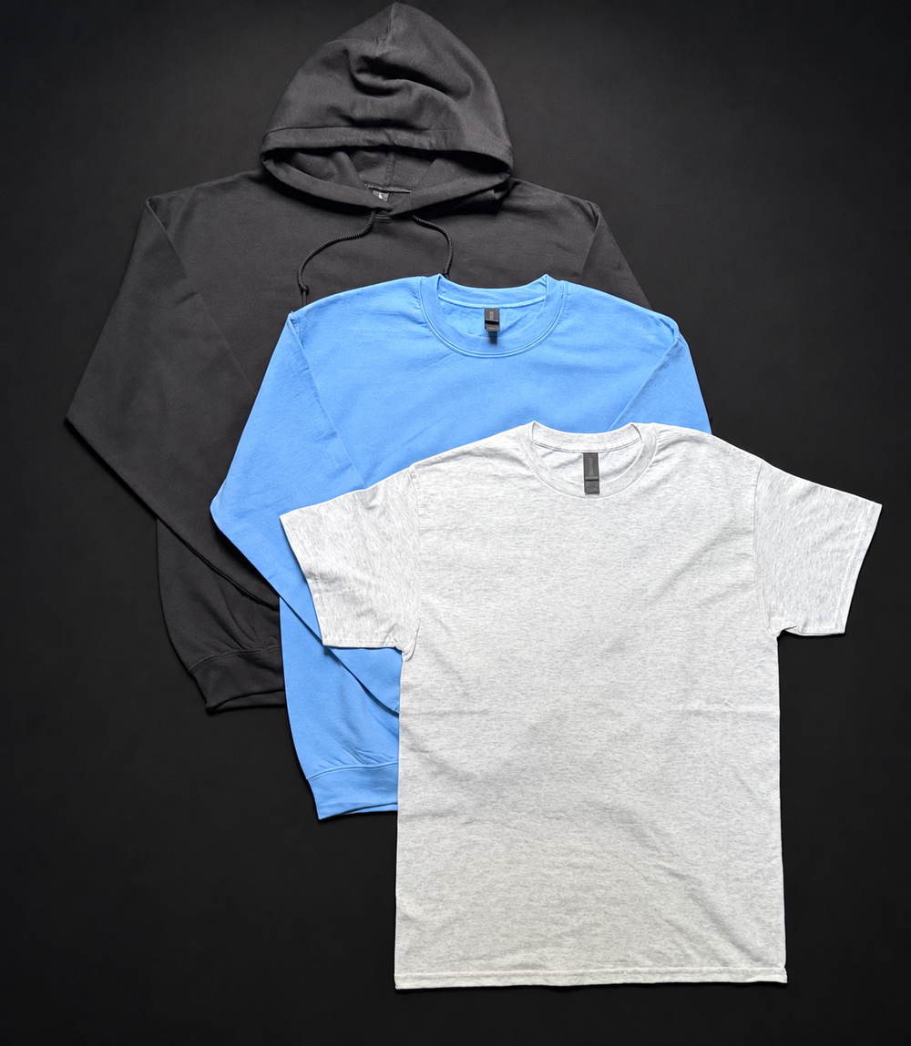 Black hoodie, blue crewneck and heather gray T-shirt on a smooth black backdrop